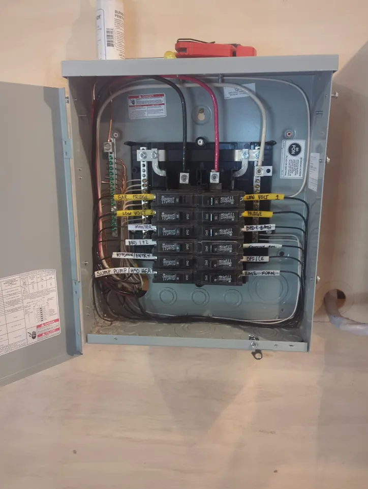 Open electrical panel showing neatly labeled circuit breakers, color-coded wires, and attached ground and neutral bars inside a metal enclosure.